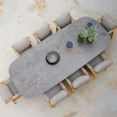 Top view of a gray oval outdoor dining table surrounded by eight dining chairs with gray cushions on a patio