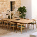 Patio dining setup with a teak oval outdoor dining table and chairs against a stone wall