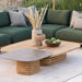 Patio lounge area with a green sectional sofa, a wooden square coffee table, and a small ceramic-top side table, with tall green grasses in the background