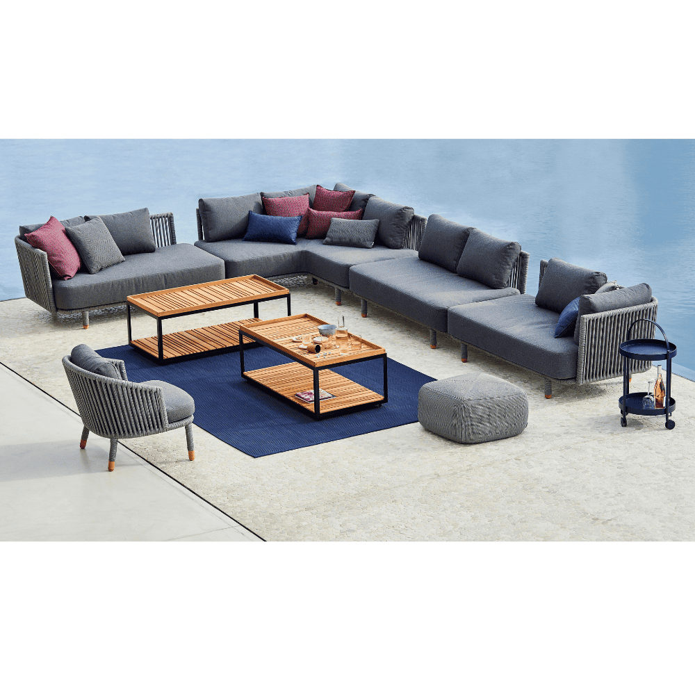 Boxhill's  Moments Outdoor Corner Module lifestyle image with other Moments Module Sofa Collection, 2 Level Coffee Table with Teak Top, Moments Outdoor Lounge Chair and a fabric footstool beside the pool