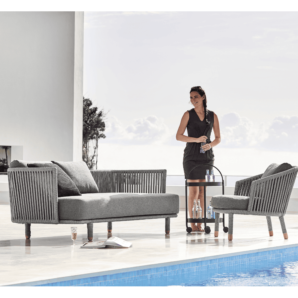Boxhill's Moments Outdoor Lounge Chair lifestyle image with a woman standing beside Moments 3-Seater Sofa at poolside