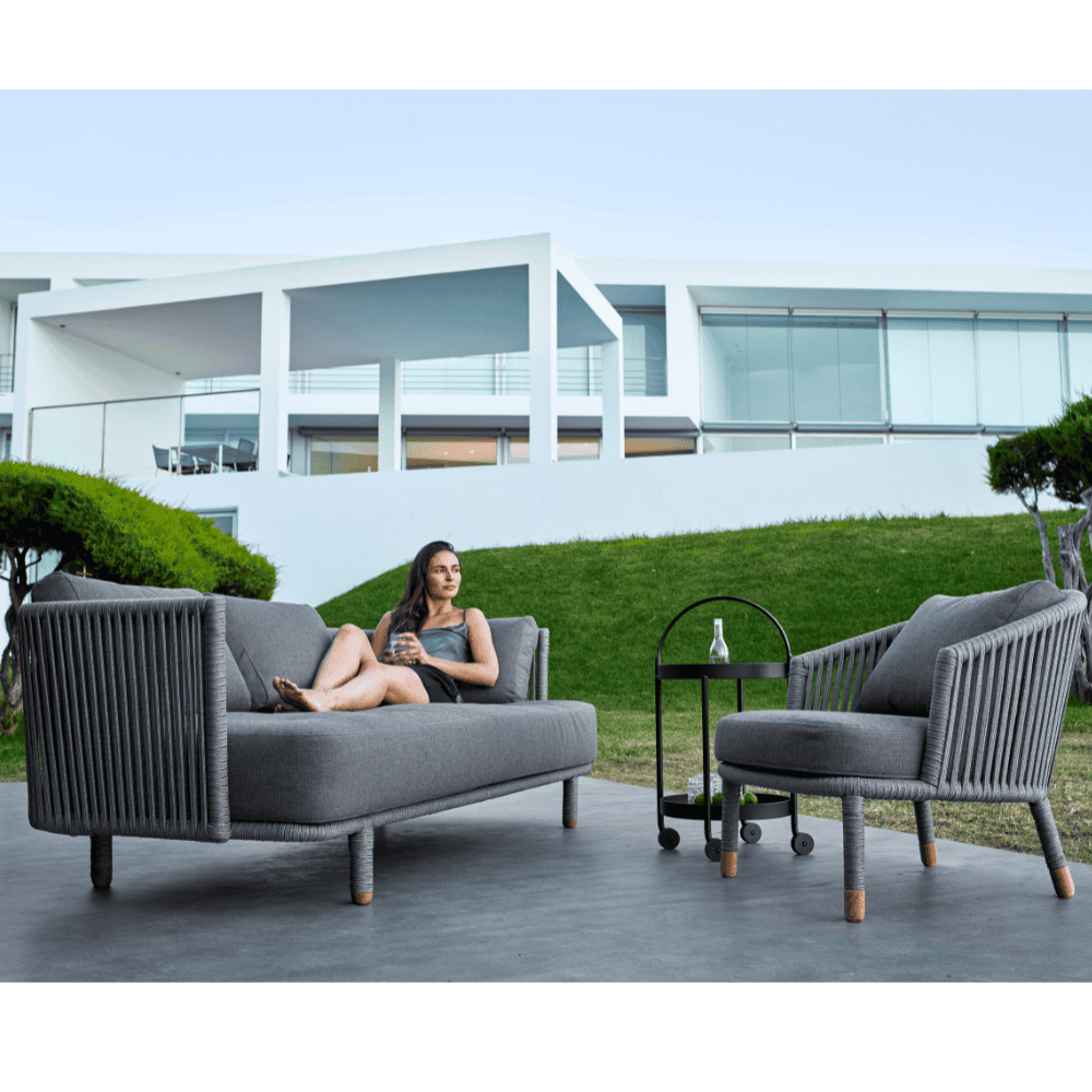 Boxhill's Moments 3-Seater Sofa lifestyle image with Moments Outdoor Lounge Chair and a relaxed woman sitting