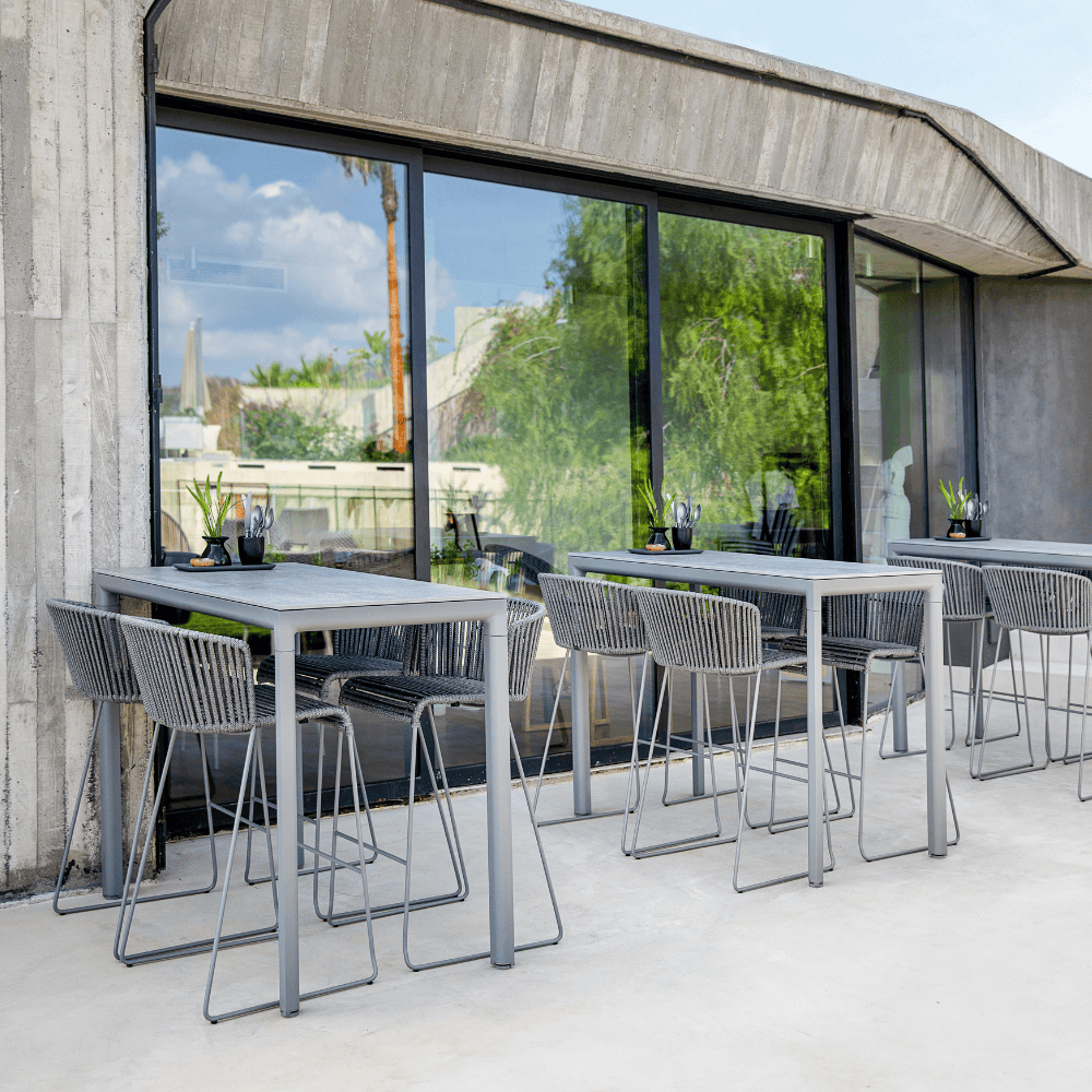 Boxhill's Moment Outdoor Bar Chair lifestyle image with bar table beside glass wall at patio
