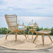 Natural rattan outdoor footstool with a matching lounge chair and side table on a seaside deck.