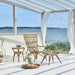 Natural rattan outdoor footstool beside a matching lounge chair and side table beneath a pergola.