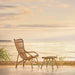 Natural rattan outdoor footstool with a matching lounge chair in a seaside sunset setting.