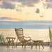Natural rattan outdoor footstool with a matching lounge chair and side table in a seaside sunset setting.