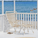 White rattan outdoor high-back lounge chair beside a matching footstool on a seaside patio.