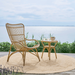 Natural rattan outdoor high-back lounge chair beside a matching side table on a round woven rug.