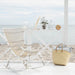 White rattan outdoor rocking chair on a seaside patio beside a woven storage basket.