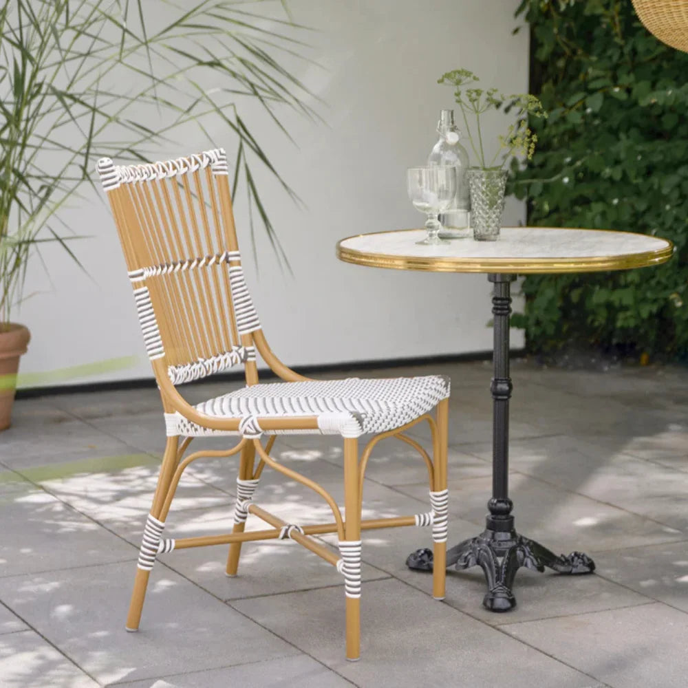 Natural rattan outdoor dining side chair with black and white woven wicker beside a round marble-top bistro table.