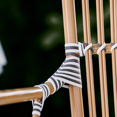 Close-up of a natural rattan outdoor bistro armchair featuring black and white woven wicker detailing.