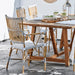 Natural rattan outdoor bistro armchair with black and white woven wicker beside a matching wooden dining table.