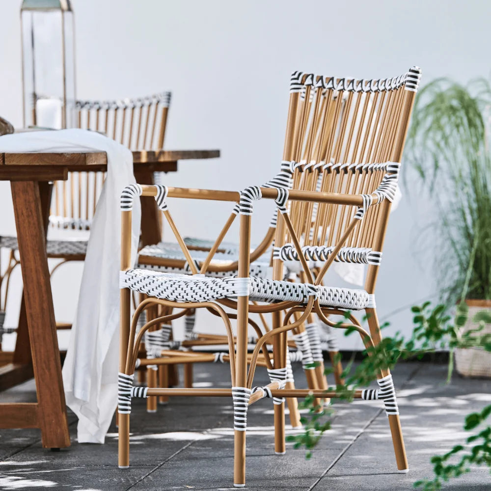 Natural rattan outdoor bistro armchair featuring black and white woven wicker beside a wooden dining table.