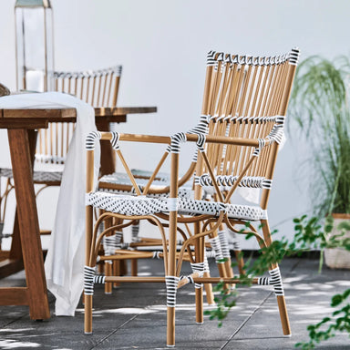 Natural rattan outdoor bistro armchair featuring black and white woven wicker beside a wooden dining table.