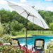 A large white patio umbrella with a dark brown pole stands beside a swimming pool in a landscaped backyard with two lounge chairs and red flowers in the foreground.