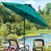 A large teal patio umbrella stands over two lounge chairs beside a swimming pool in a landscaped backyard with trees and greenery.