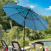 A light blue patio umbrella with a black pole and ribs, set up in a backyard garden scene next to lounge chairs and a swimming pool.