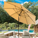 A large beige patio umbrella with a black pole and canopy ribs, set up in a backyard poolside scene with patio chairs, trees, and a swimming pool in the background.
