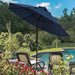 A large navy blue patio umbrella is shown in a backyard poolside setting, shading two lounge chairs with plants and trees in the background.