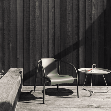 A powder coated steel dark gray outdoor lounge chair and a white outdoor tray table set on a wooden deck against wooden wall