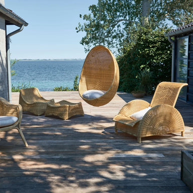 Natural rattan outdoor hanging egg chair with a white cushion among matching lounge furniture.