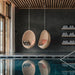 Natural rattan outdoor hanging egg chairs with cushions in a modern indoor pool setting.
