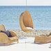 Natural rattan outdoor hanging egg chair with a white cushion beside a matching lounge chair and footstool.
