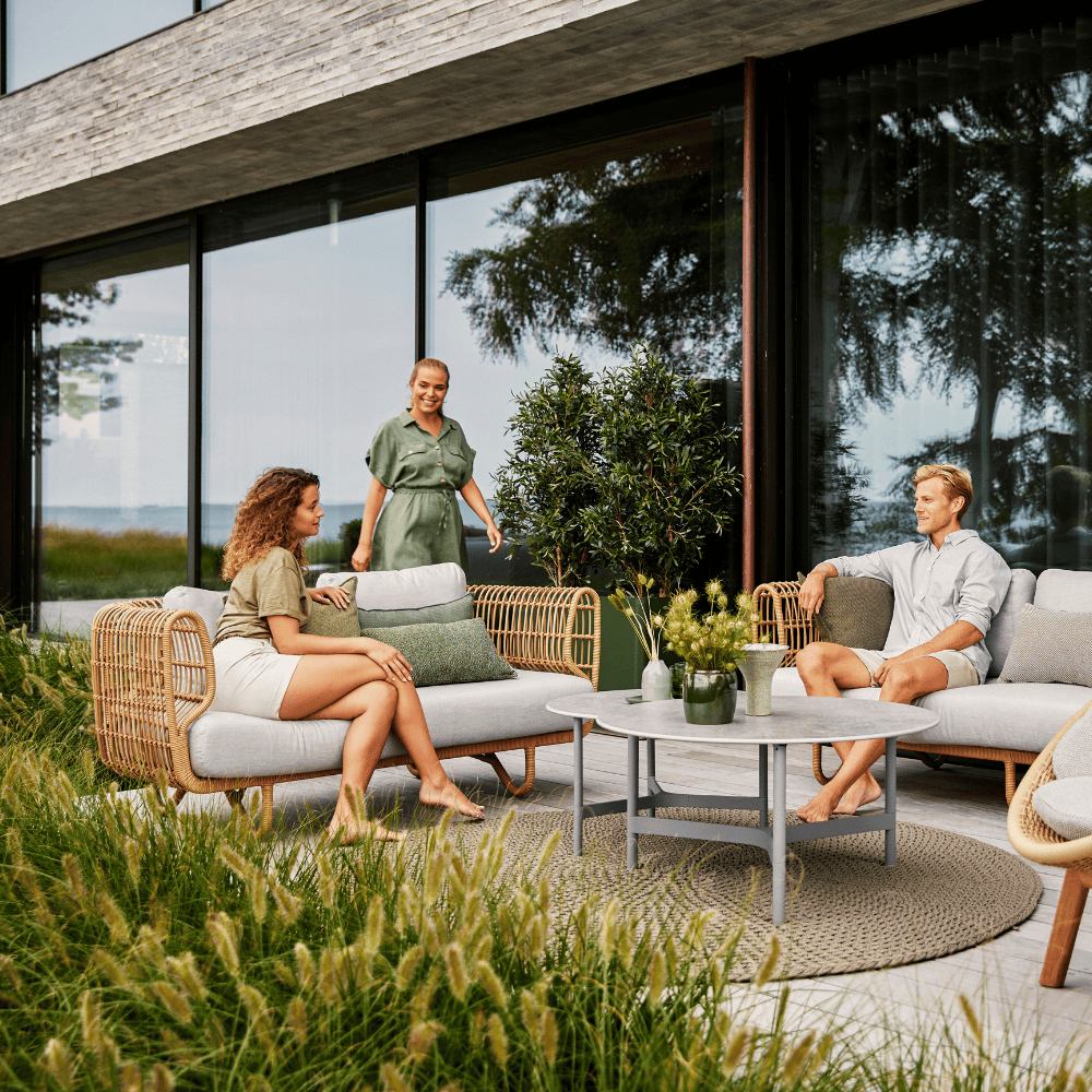 Boxhill's Nest 2-Seater Sofa lifestyle image at patio with man and a woman sitting down having a chat, and another woman walking at the side