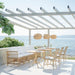 Round teak outdoor café table beside a matching sofa and natural rattan dining side armchairs on a seaside patio.
