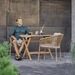 Boxhill's Ocean Outdoor Dining Armchair lifestyle image at patio with teak table and a man sitting holding a cup of coffee