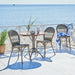 Gray rattan outdoor dining side chair beside a round teak café table on a seaside patio.
