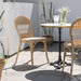 Natural rattan outdoor dining side chair beside a round teak café table on a sunny patio.