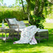 Gray rattan outdoor chaise lounge with white cushions beside a matching side table in a garden.