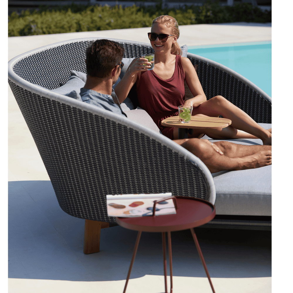 Boxhill's On-The-Move maroon outdoor round side table beside grey outdoor daybed with man and a woman sitting on it