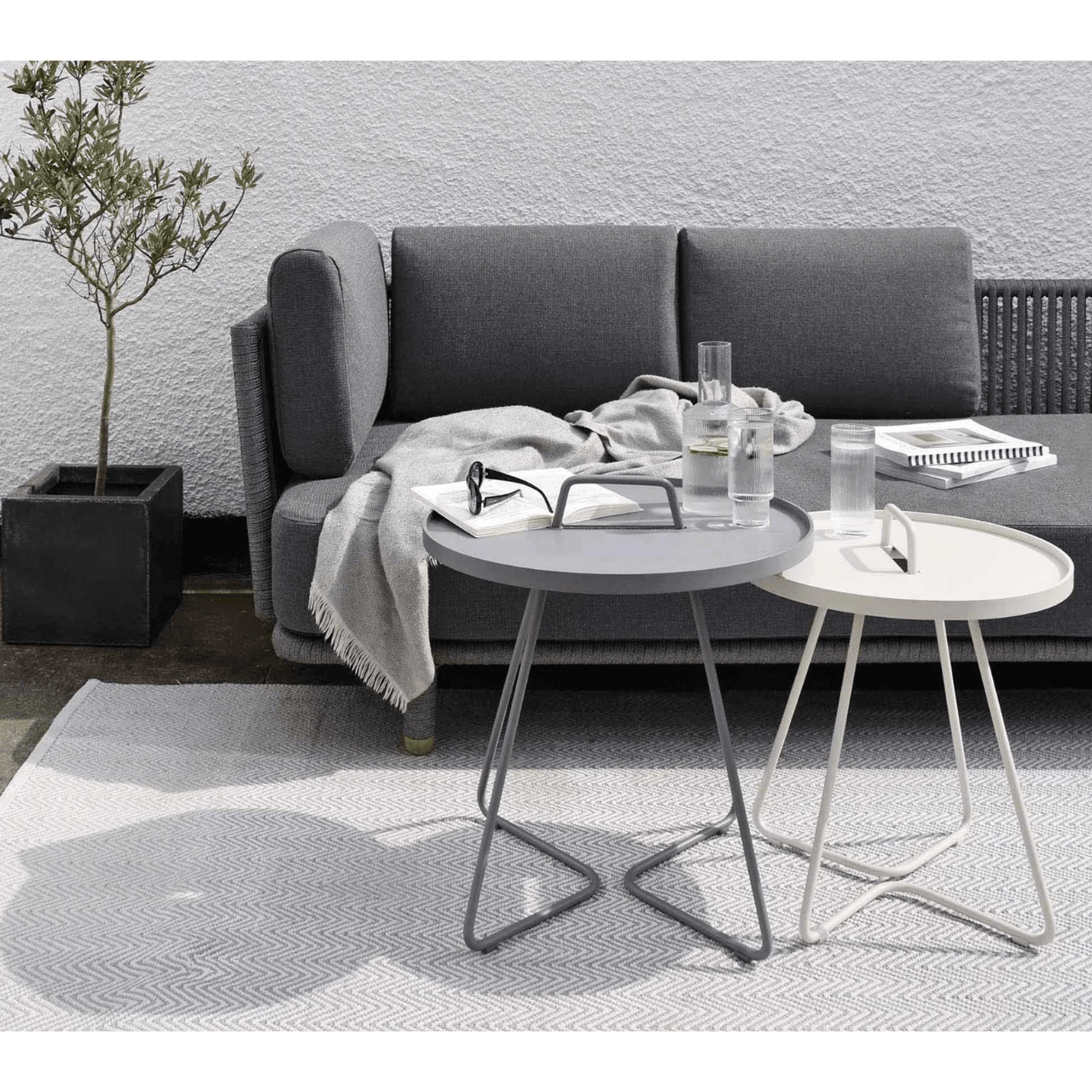 Boxhill's On-The-Move light grey and white outdoor round side table infront of charcoal grey 3-seater outdoor sofa placed in patio