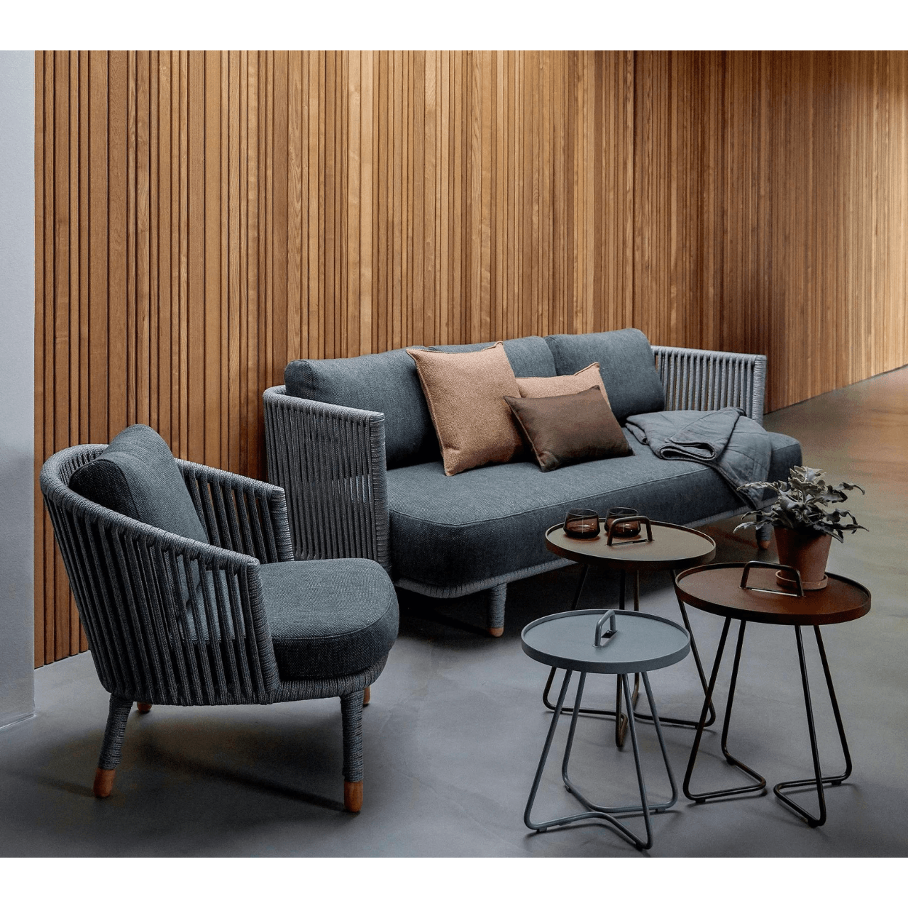 Boxhill's On-The-Move light grey and brown outdoor round side table, grey outdoor lounge chair and grey outdoor sofa placed against wooden wall