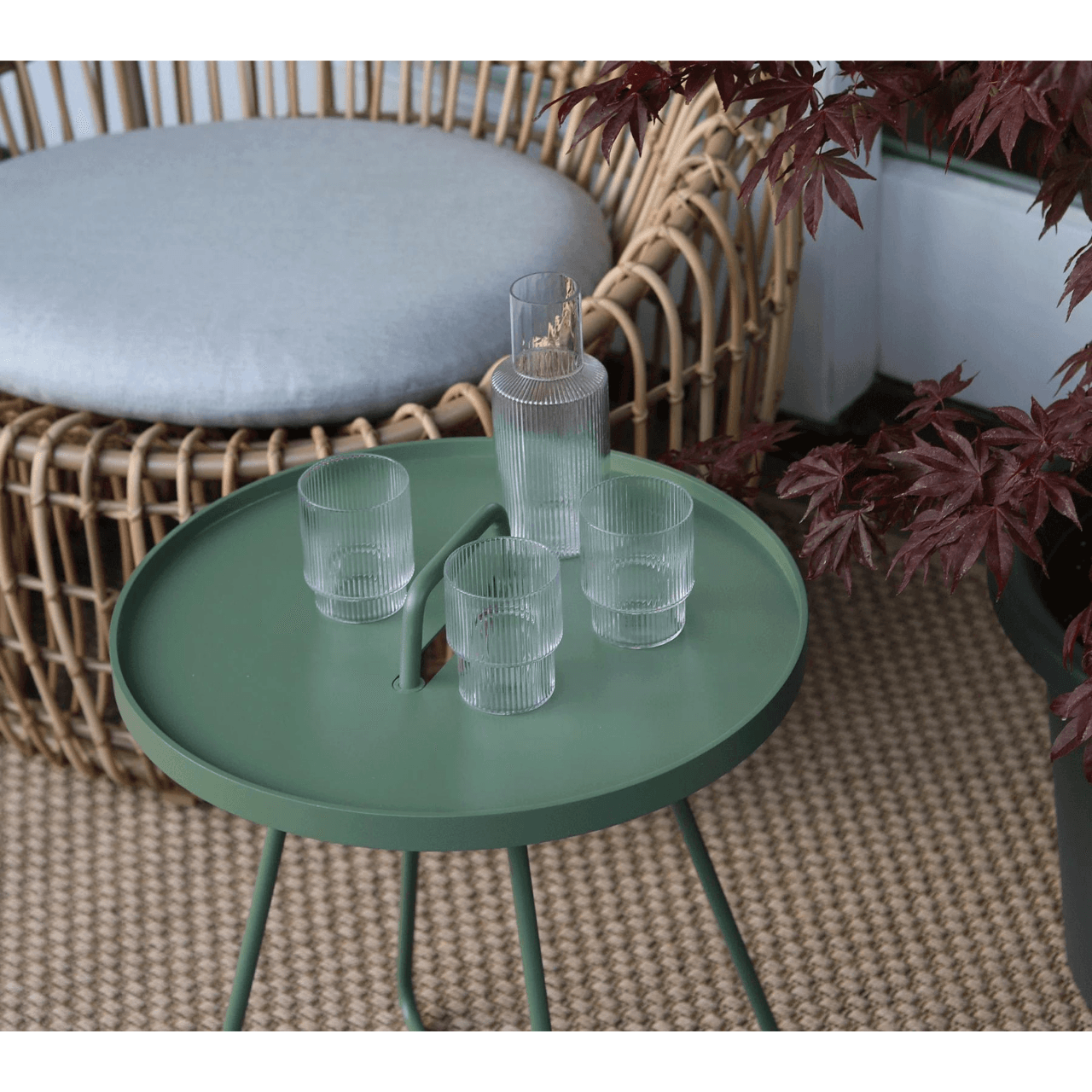 Boxhills On-The-Move olive green outdoor round side table with glasses of water and bottle on it beside outdoor round rattan chair