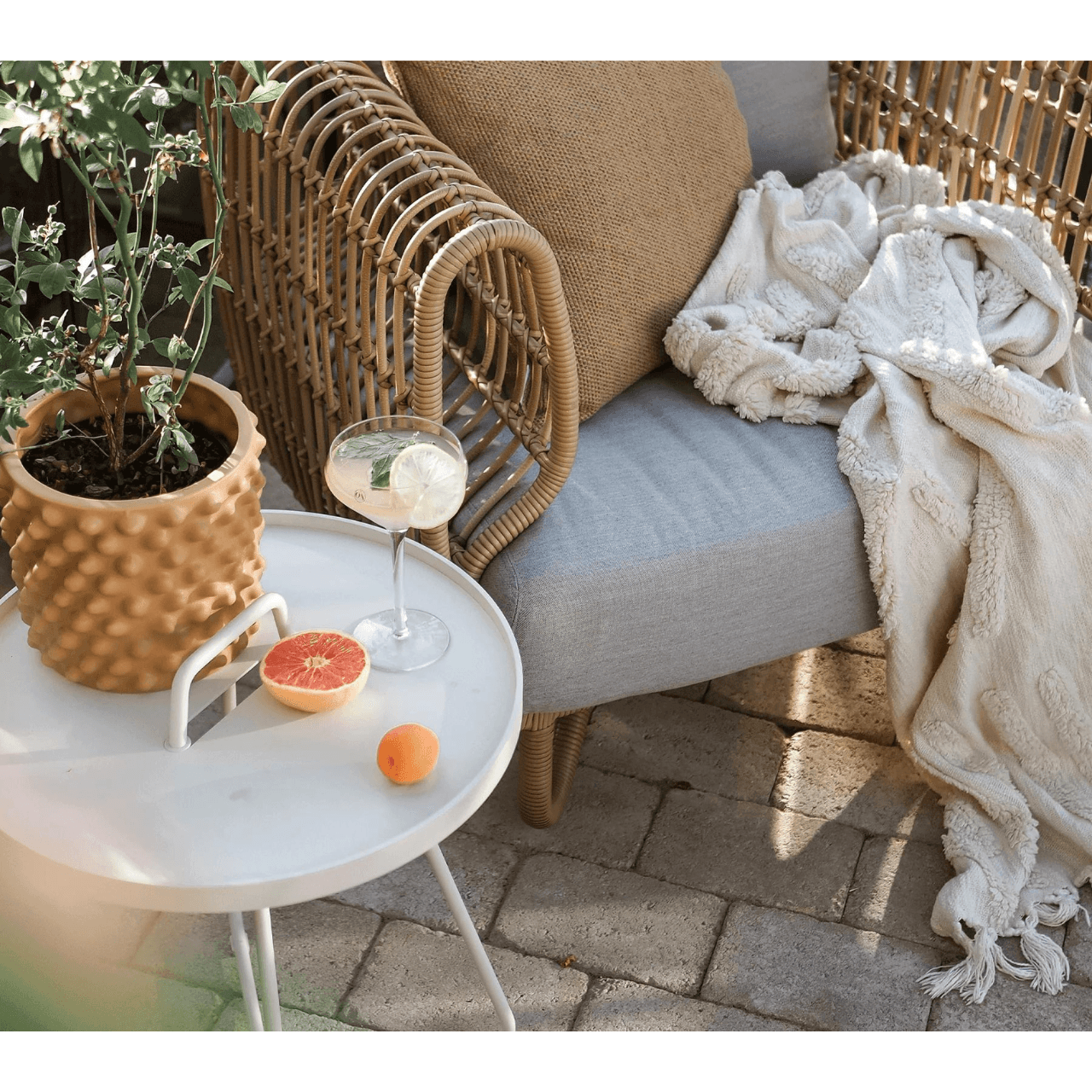  Boxhill's On-The-Move white outdoor round side table with glass of lemonade and plants on it beside Nest outdoor lounge chair