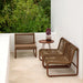 Two wicker chairs and an outdoor small  side table on a patio with greenery in the background.
