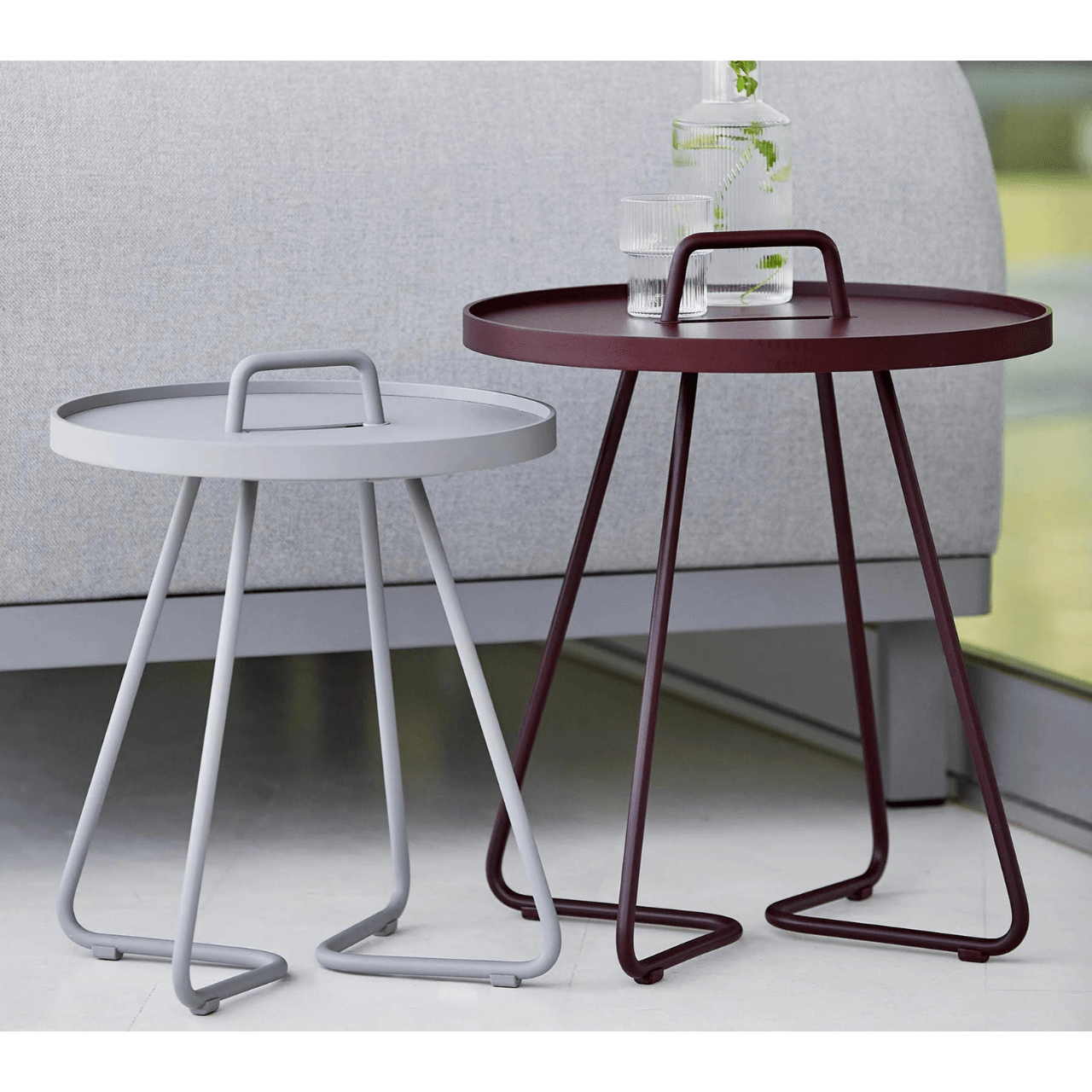 Boxhill's On-The-Move light grey and maroon outdoor round side table with glass of water and a bottle container on it