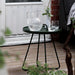 Dark green outdoor side table with a crystal pitcher and glasses on a wooden deck.