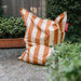 Orange and beige striped bean bag chair with a Fatboy tag on a stone surface with greenery.