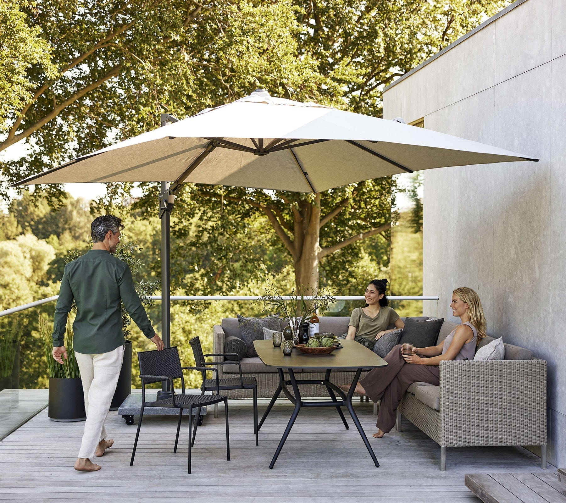 Boxhill's Connect Dining Lounge Combo A Taupe cushion lifestyle image with big umbrella sunshade on balcony with 2 women sitting down and a man standing beside