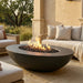 Outdoor patio with outdoor conrete oval fire pit, seating area, and natural landscape