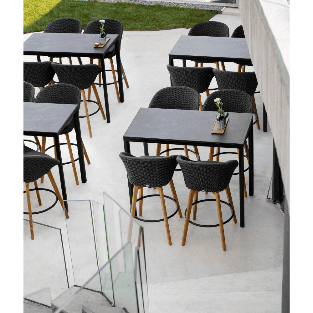 Boxhill's Peacock dark grey outdoor bar chair with teak legs and black outdoor bar table placed near the stairs