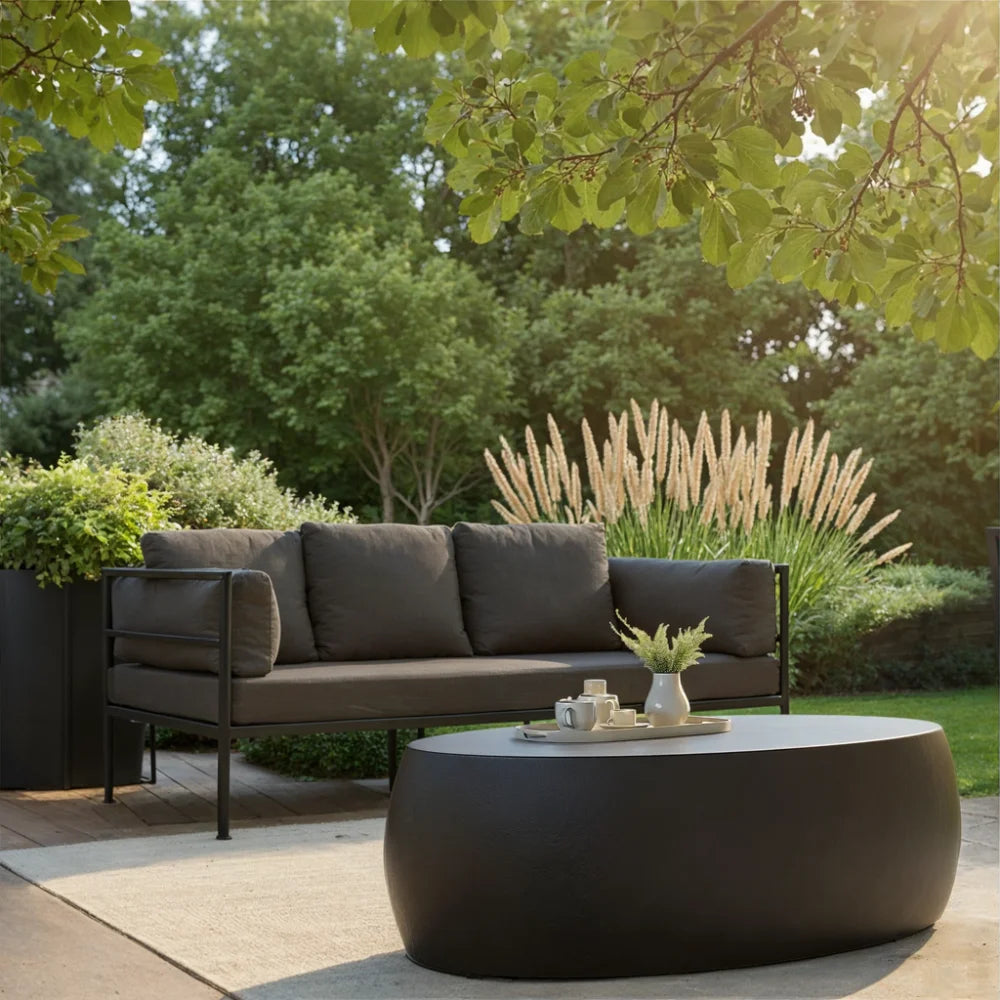 Patio seating with black pebble concrete outdoor coffee table on light beige rug, dark gray sofa, surrounded by greenery