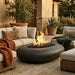 Outdoor patio with black concrete oval fire pit, chairs, and plants