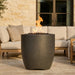 Tall cylinder-shaped outdoor concrete fire pit in front of a patio with a couch and cushions