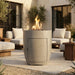 Outdoor patio setting with a tall cylindrical outdoor conrete fire pit with hidden propane enclosure door and seating area.